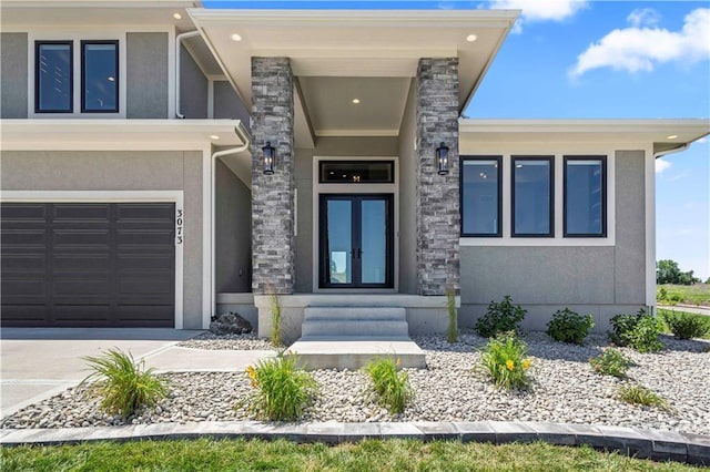 property entrance featuring stone siding, stucco siding, french doors, an attached garage, and driveway