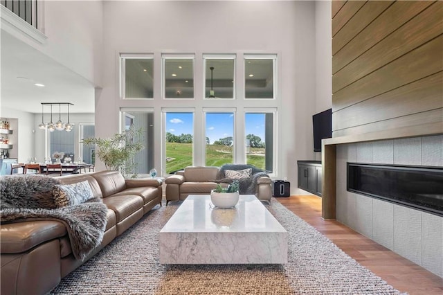 living area featuring a tiled fireplace, a healthy amount of sunlight, wood finished floors, and a towering ceiling