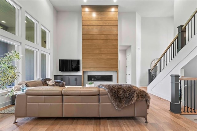 living room with wood finished floors, baseboards, a glass covered fireplace, and a high ceiling