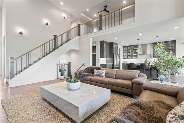 living room with a towering ceiling, recessed lighting, wood finished floors, and stairs