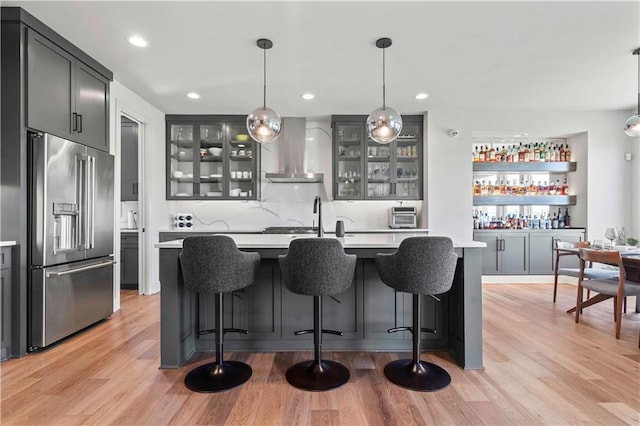 bar with wet bar, hanging light fixtures, wall chimney exhaust hood, high end refrigerator, and light wood-style flooring