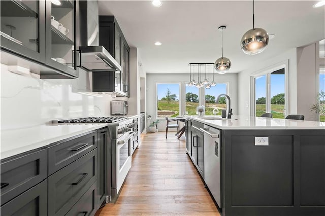 kitchen with a sink, wall chimney exhaust hood, a healthy amount of sunlight, and stainless steel appliances