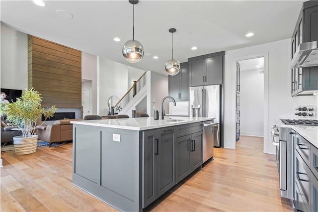 kitchen with wall chimney range hood, a sink, light wood finished floors, a fireplace, and high end appliances