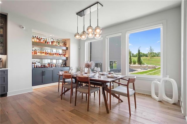 dining space featuring bar, visible vents, baseboards, a notable chandelier, and light wood-style flooring
