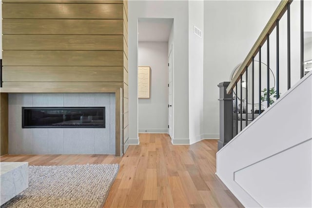 foyer entrance featuring visible vents, stairs, wood finished floors, baseboards, and a tiled fireplace