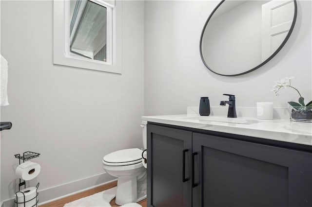 half bath featuring toilet, baseboards, wood finished floors, and vanity
