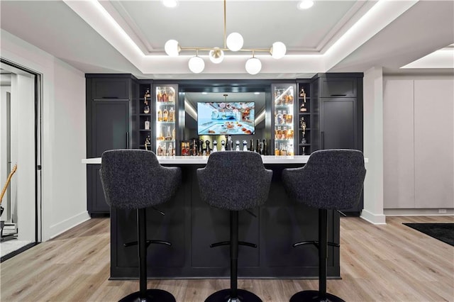 bar with baseboards, a raised ceiling, light wood finished floors, and bar