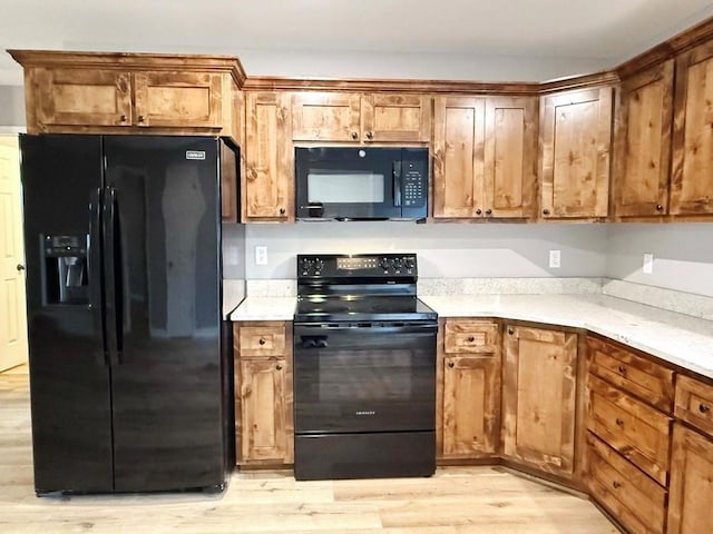 kitchen with light countertops, brown cabinetry, black appliances, and light wood-type flooring