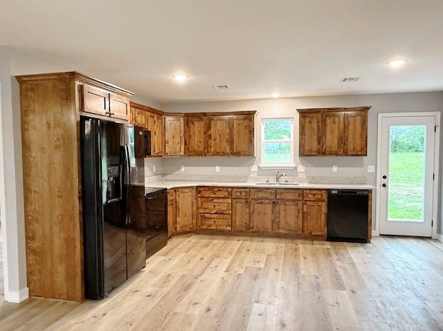 kitchen with a sink, brown cabinetry, black appliances, and light wood-style flooring