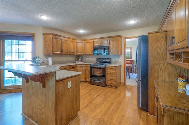 14241 W 113th Ter, Olathe, KS 66062 - kitchen featuring black appliances, a peninsula, light wood-type flooring, brown cabinets, and a textured ceiling