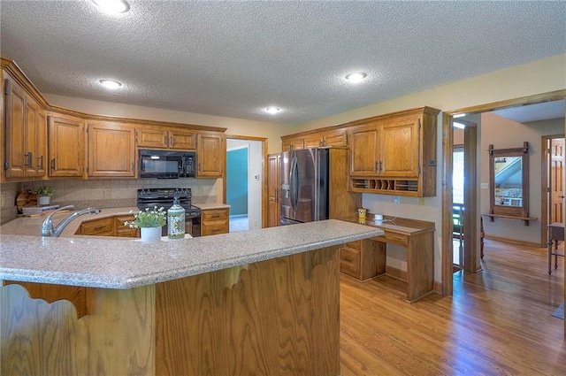 14241 W 113th Ter, Olathe, KS 66062 - kitchen with black appliances, light wood finished floors, a sink, a textured ceiling, and a peninsula