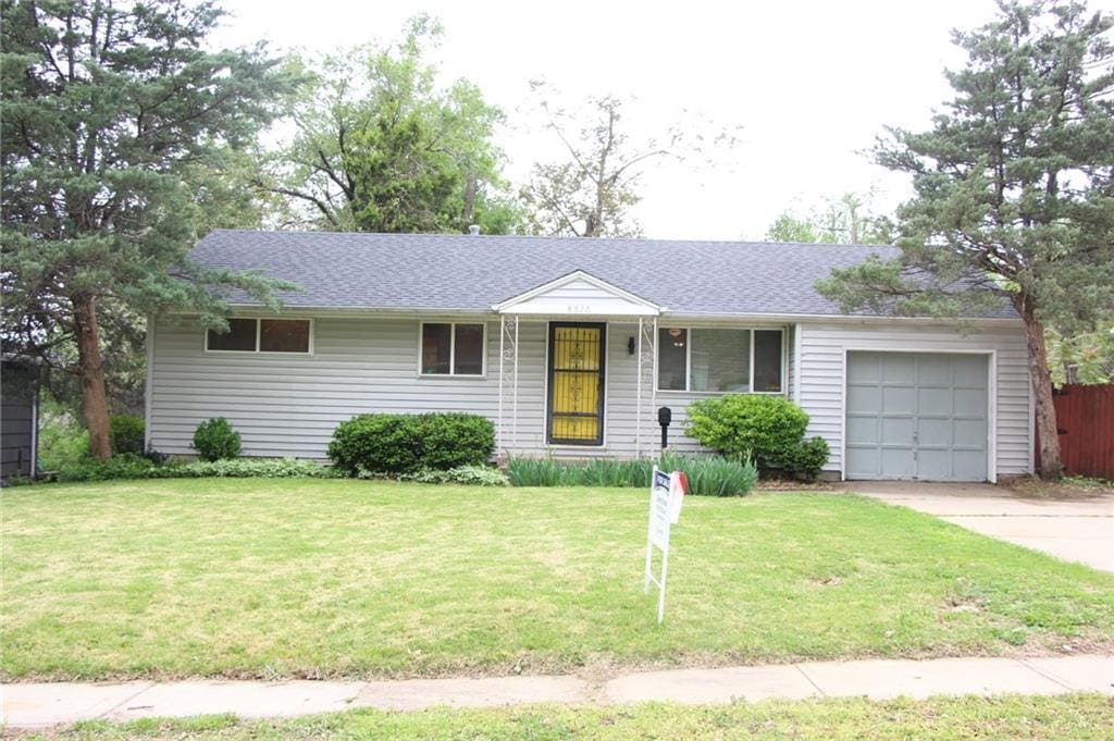ranch-style house with driveway, fence, a front lawn, an attached garage, and a shingled roof