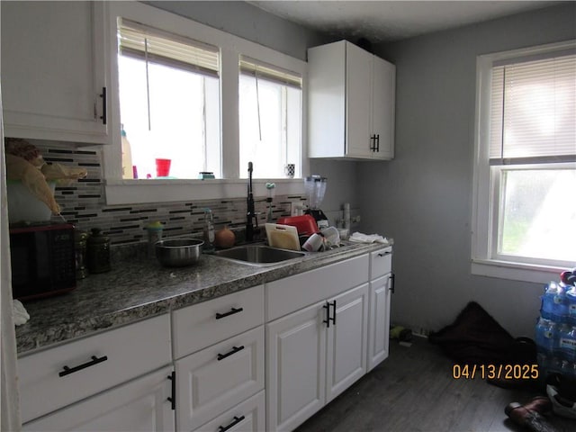 kitchen with backsplash, dark wood-style flooring, black microwave, a sink, and white cabinets