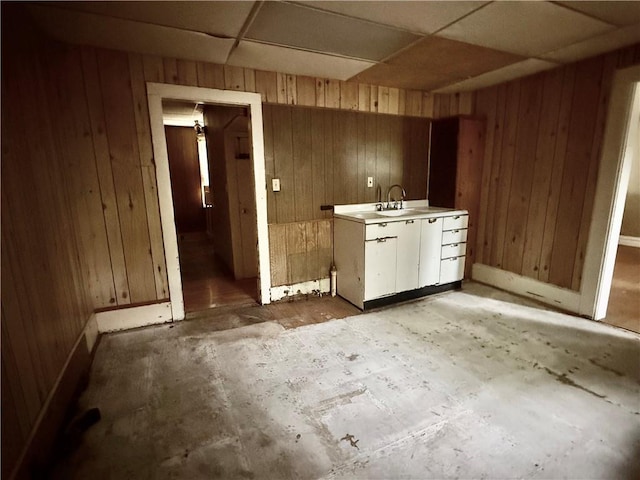 interior space with baseboards, a sink, a drop ceiling, and wooden walls