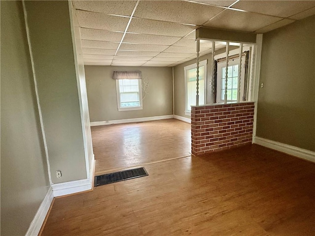 empty room featuring visible vents, a paneled ceiling, baseboards, and wood finished floors