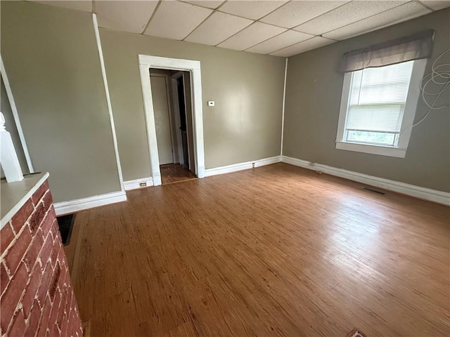 unfurnished room with baseboards, a paneled ceiling, wood finished floors, and visible vents