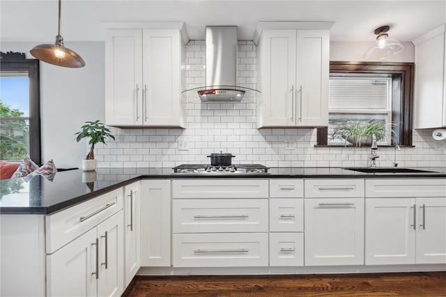 3804 Harrison St, Kansas City, MO 64109 - kitchen featuring wall chimney range hood, white cabinets, a sink, a peninsula, and stainless steel gas stovetop