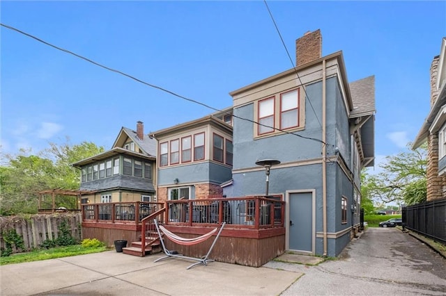 3804 Harrison St, Kansas City, MO 64109 - rear view of house with a chimney, stucco siding, a deck, and fence