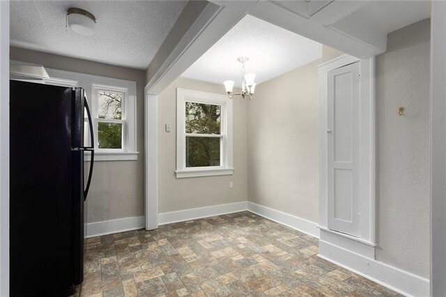 708 N River Blvd, Independence, MO 64050 - unfurnished dining area featuring baseboards, a textured ceiling, stone finish floor, and an inviting chandelier