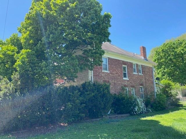 view of side of property with a lawn, brick siding, and a chimney