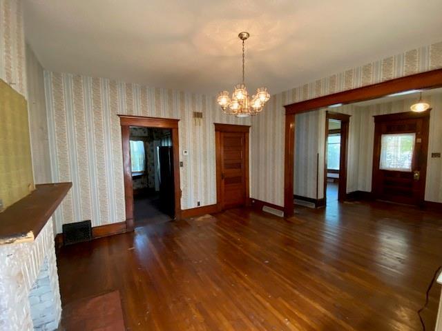 unfurnished dining area featuring wallpapered walls, a chandelier, and wood finished floors