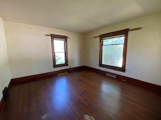 unfurnished room featuring baseboards, dark wood-style flooring, and visible vents