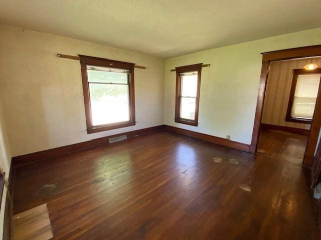 empty room with baseboards, a textured ceiling, and dark wood-style floors