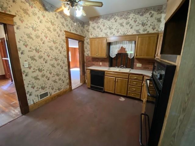 kitchen with a sink, ceiling fan, black dishwasher, and wallpapered walls