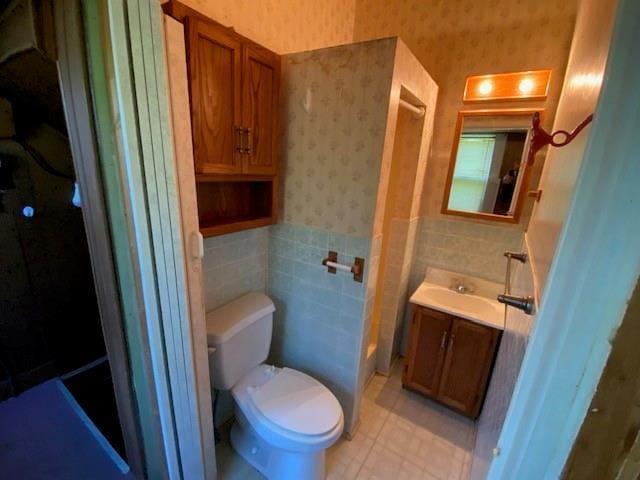bathroom with vanity, wainscoting, toilet, and wallpapered walls