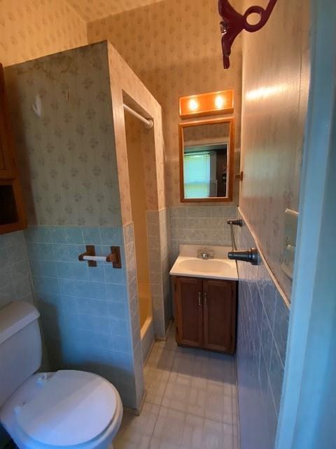 full bath with wainscoting, vanity, toilet, wallpapered walls, and tile walls