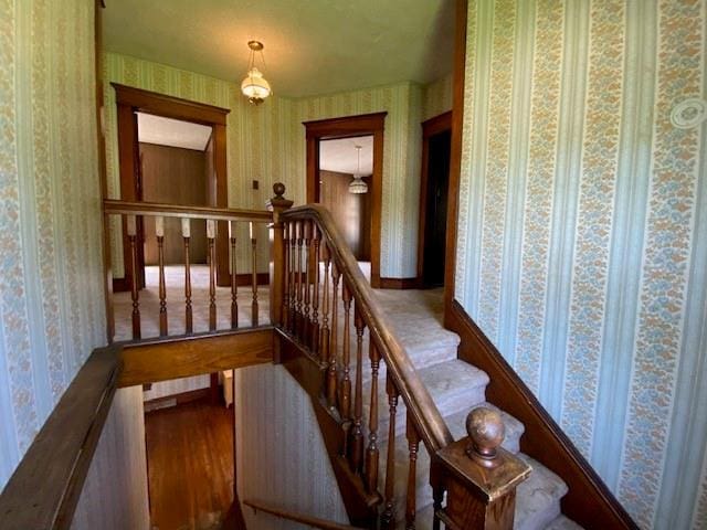 staircase with wallpapered walls and wood finished floors