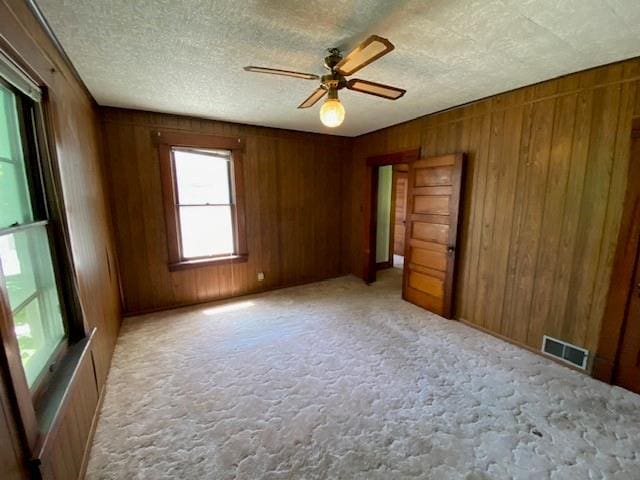 interior space with visible vents, a ceiling fan, and wooden walls