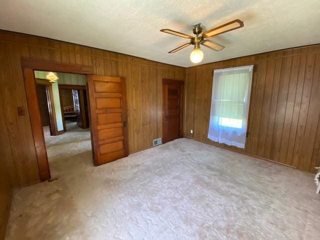 carpeted empty room with ceiling fan, wood walls, and visible vents