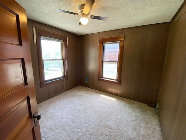 empty room featuring wooden walls, a ceiling fan, a textured ceiling, and plenty of natural light