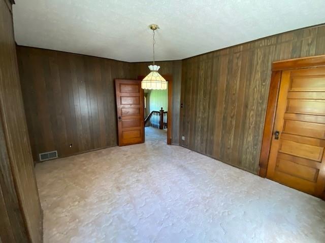 carpeted spare room featuring wood walls and visible vents