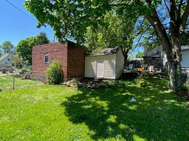 view of side of home featuring fence, an outbuilding, a lawn, and a storage shed
