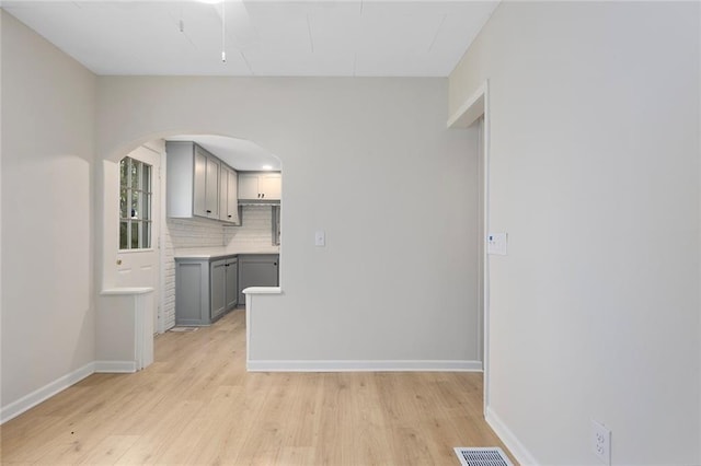 4433 N Jackson Ave, Kansas City, MO 64117 - interior space featuring gray cabinets, backsplash, arched walkways, baseboards, and light wood-style flooring
