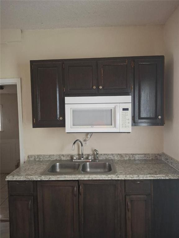 104 S 13th St, Kansas City, KS 66102 - kitchen featuring white microwave, a sink, light countertops, dark brown cabinets, and a textured ceiling