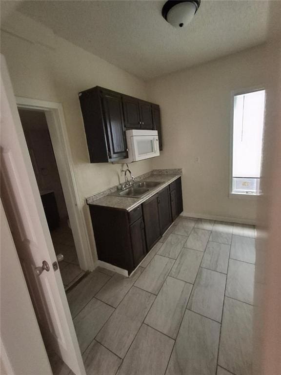 104 S 13th St, Kansas City, KS 66102 - kitchen with a sink, white microwave, light countertops, baseboards, and dark cabinetry