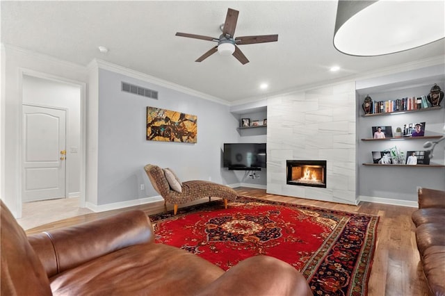living area with visible vents, crown molding, wood finished floors, ceiling fan, and a tiled fireplace