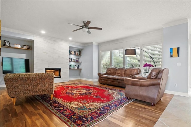 living room featuring ornamental molding, wood finished floors, baseboards, a tile fireplace, and a ceiling fan