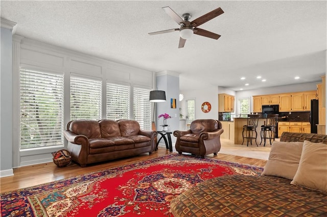 living area with recessed lighting, a ceiling fan, light wood-type flooring, and a textured ceiling