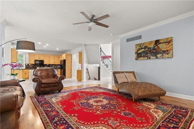 living area featuring crown molding, light wood-style flooring, stairs, a ceiling fan, and visible vents