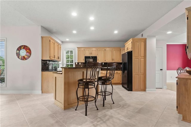 kitchen with light brown cabinets, dark countertops, a breakfast bar area, recessed lighting, and black appliances