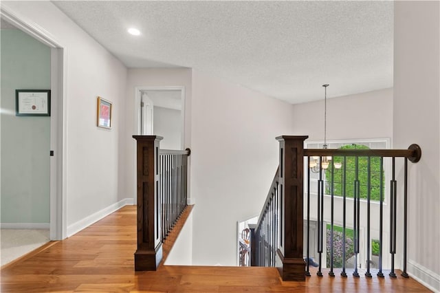 staircase with wood finished floors, baseboards, recessed lighting, a textured ceiling, and a chandelier