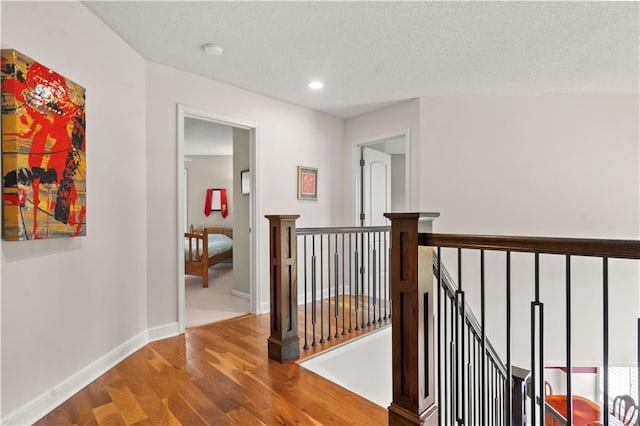 corridor with baseboards, recessed lighting, wood finished floors, and an upstairs landing