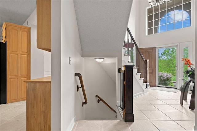 stairs with tile patterned floors, a chandelier, baseboards, and a towering ceiling