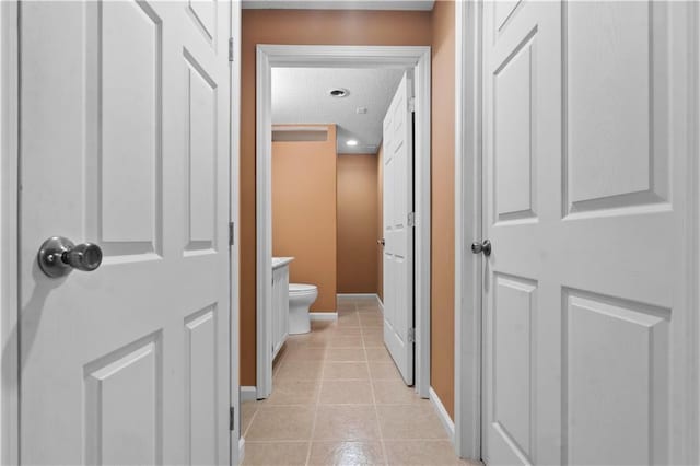 hallway with baseboards, a textured ceiling, and light tile patterned floors