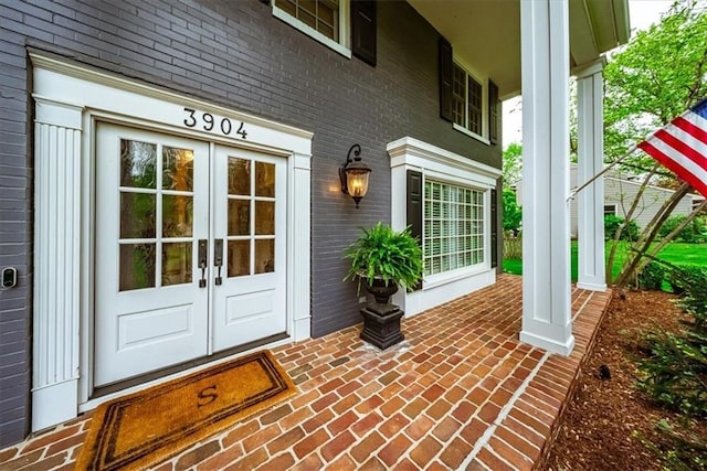 property entrance featuring covered porch, brick siding, and french doors