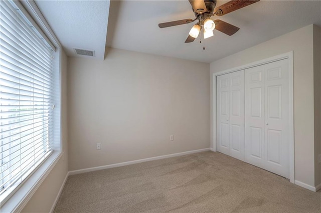unfurnished bedroom featuring ceiling fan, visible vents, baseboards, a closet, and light carpet